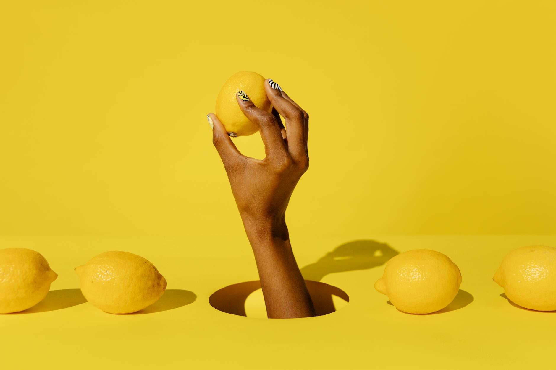 A hand holding a fresh lemon against a bright yellow background, symbolizing new beginnings and exploration
