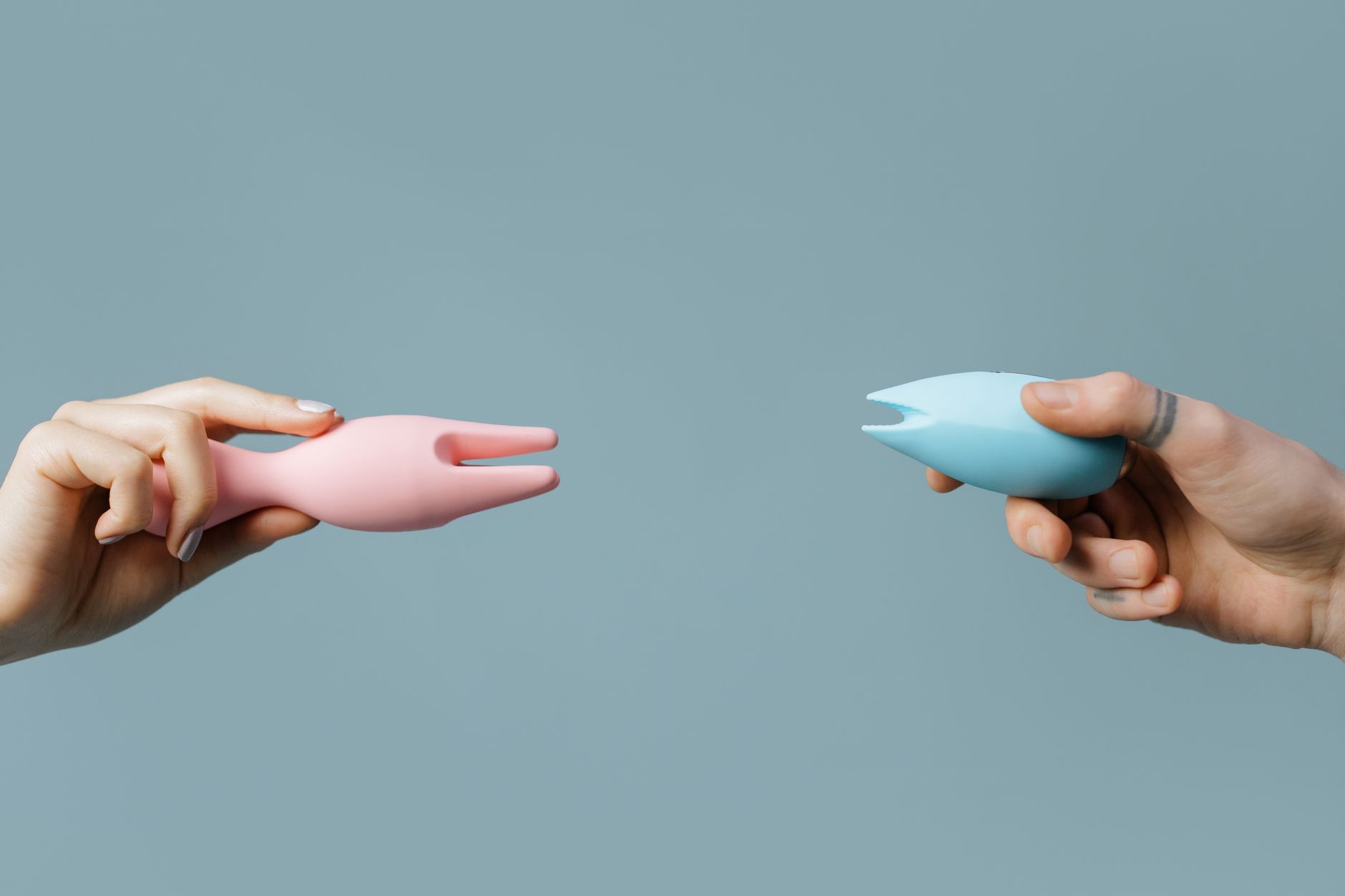 Hands holding colorful silicone vibrators against a soft pastel background, representing sensitive pleasure.