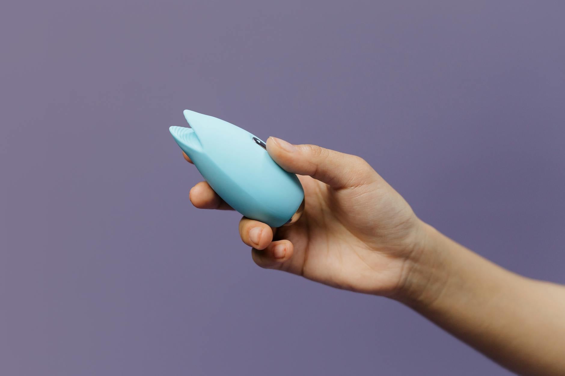 A blue silicone adult toy held in hand against a solid purple background, promoting self-love and sexuality