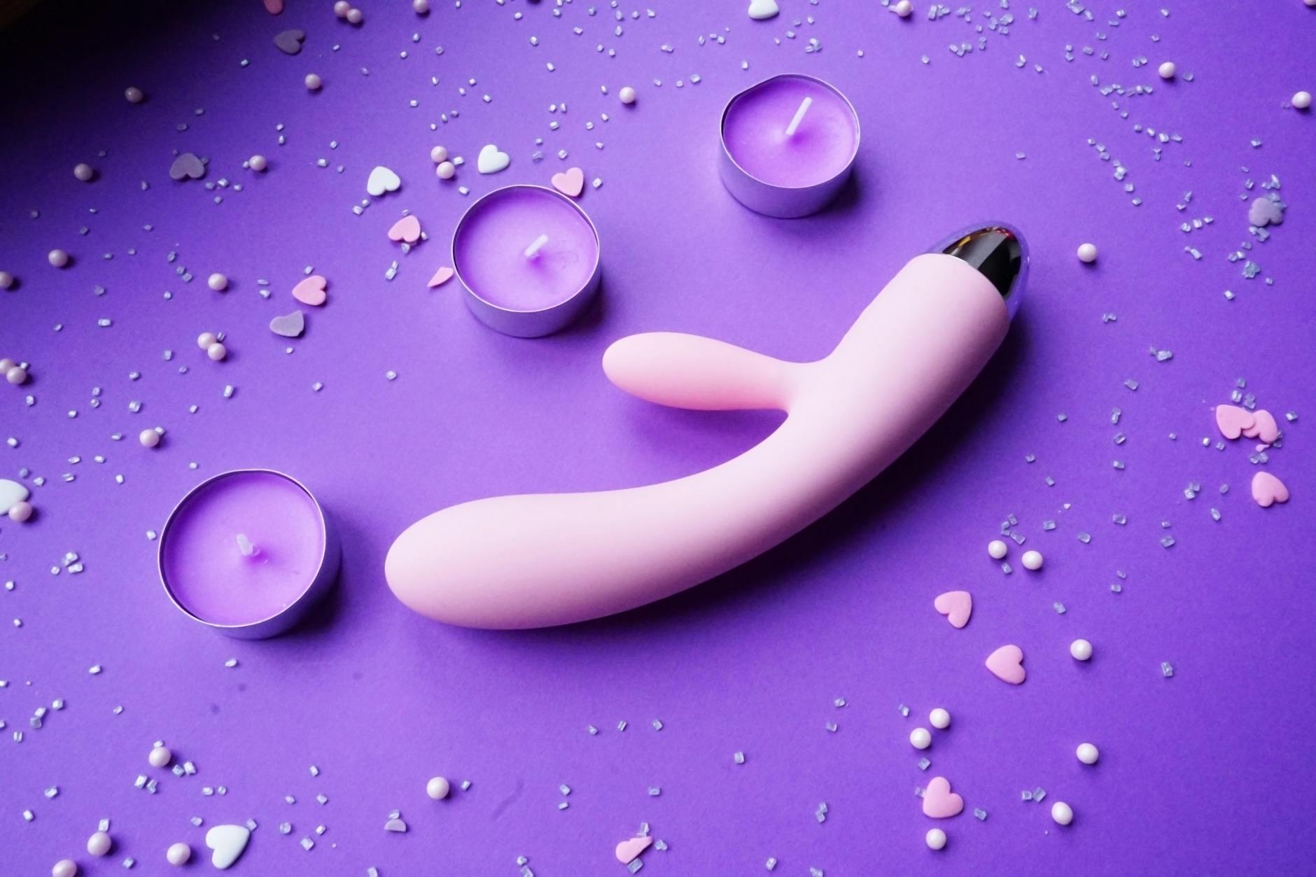 Pink vibrator on purple background with heart confetti and candles for a romantic intimate setting