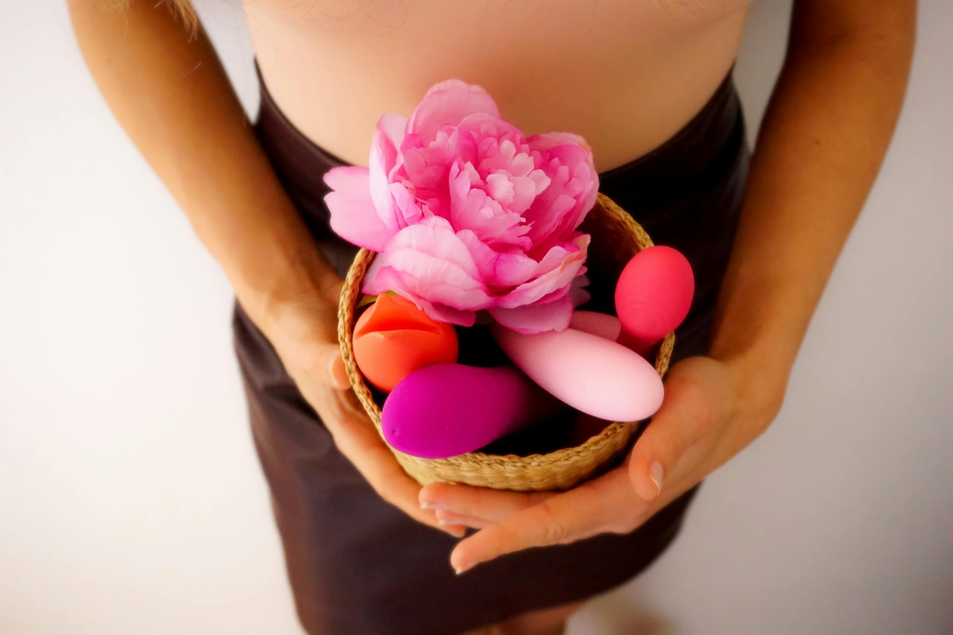 Two hands holding silicone vibrators against a soft pastel background
